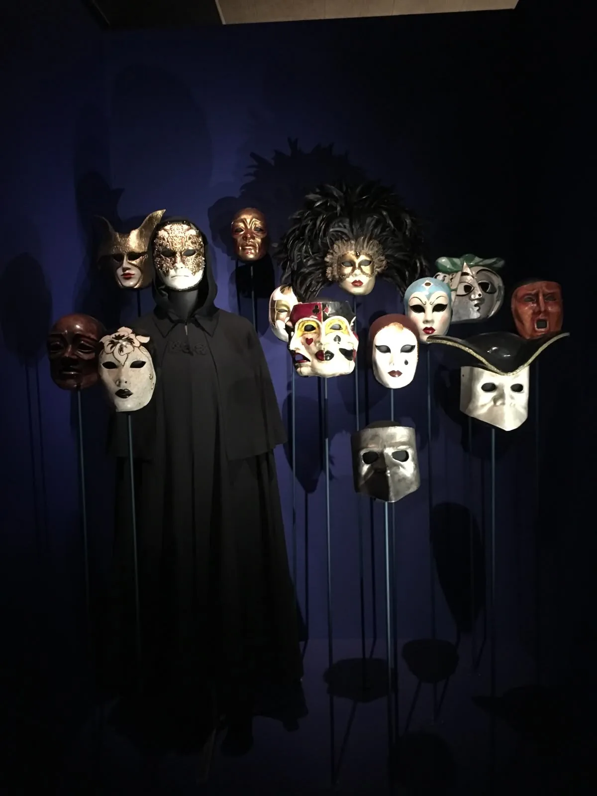 Masks on display, a cloaked figure among them